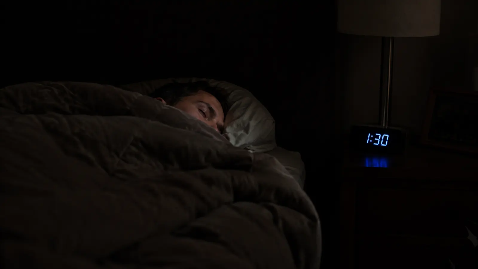 Person reading a book peacefully under a weighted blanket on a couch in a dimly lit living room