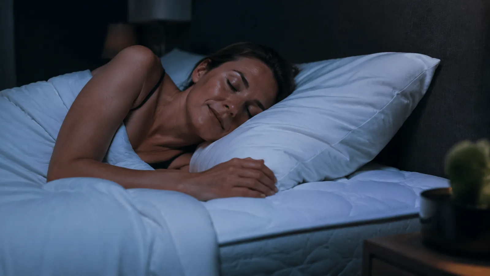 A bedroom at night with a fan running and sheets pushed to the edge of the bed, empty and disheveled